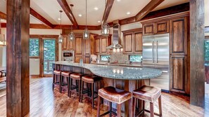 A spacious kitchen with wooden cabinets, a large island with stools, and stainless steel appliances. - Breck_rocky_mtn_lodge (Breckenridge)