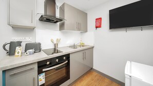 Une cuisine moderne équipée d’un four encastré, d’un micro-ondes et d’une machine à café. On y trouve un évier avec un robinet et un égouttoir à vaisselle. La cuisine est dotée de meubles gris clair et d’un plan de travail blanc.