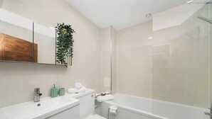 Une salle de bain moderne avec un grand miroir, un lavabo blanc, des toilettes et une baignoire.