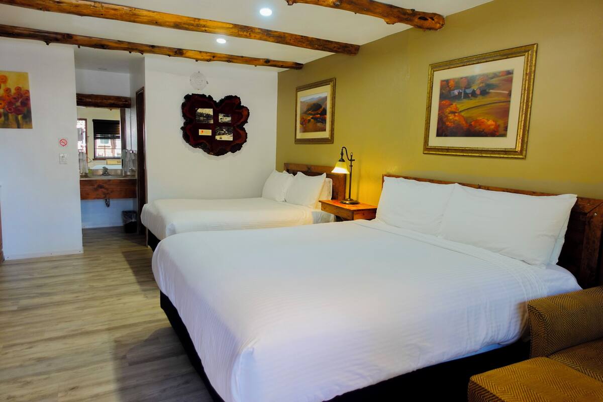 Ein Hotelzimmer mit zwei Betten, Holzbalken an der Decke und gerahmten Kunstwerken an den Wänden.