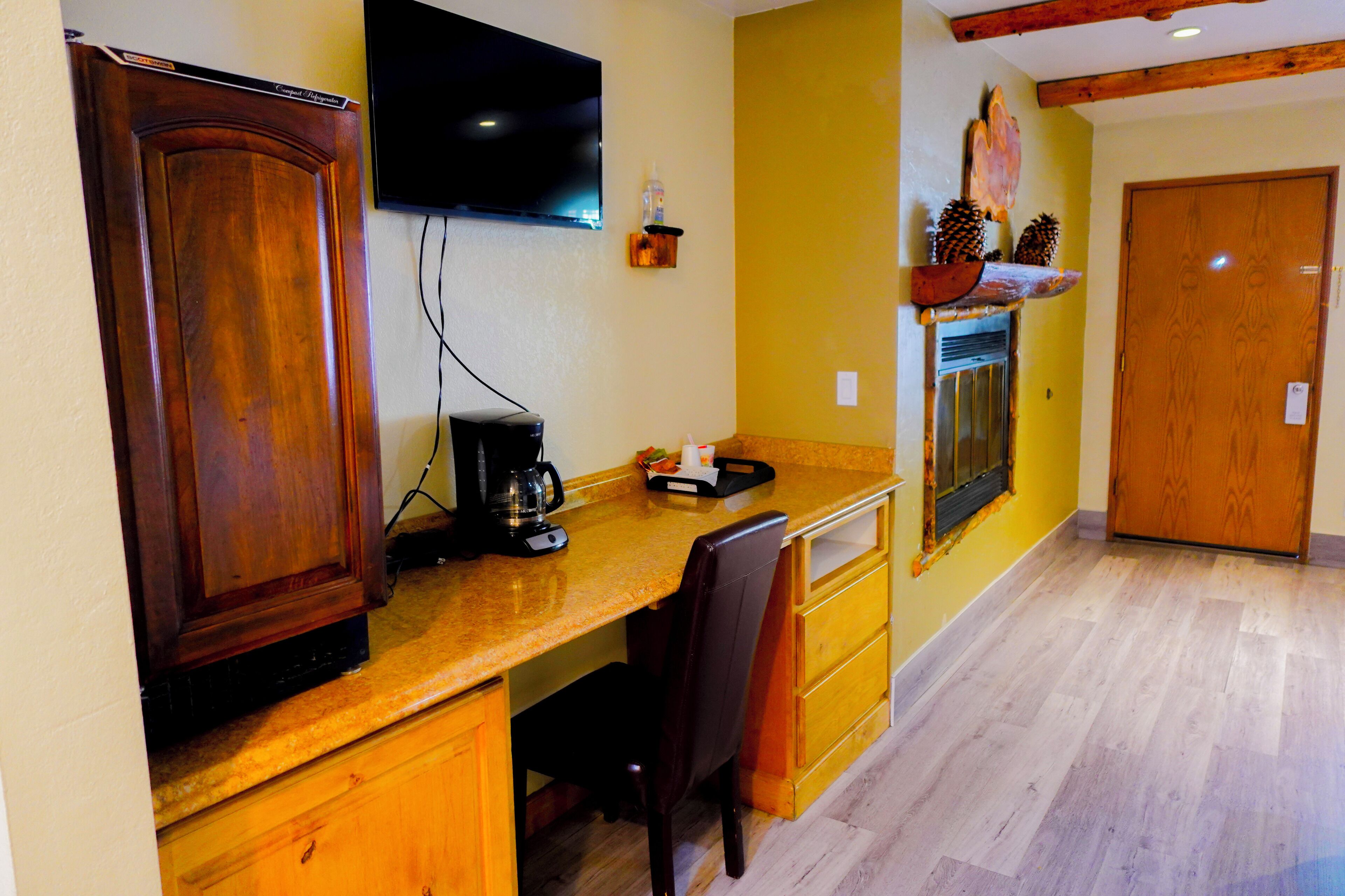 A kitchen with wooden cabinets, a countertop, a coffee maker, and a television mounted on the wall.