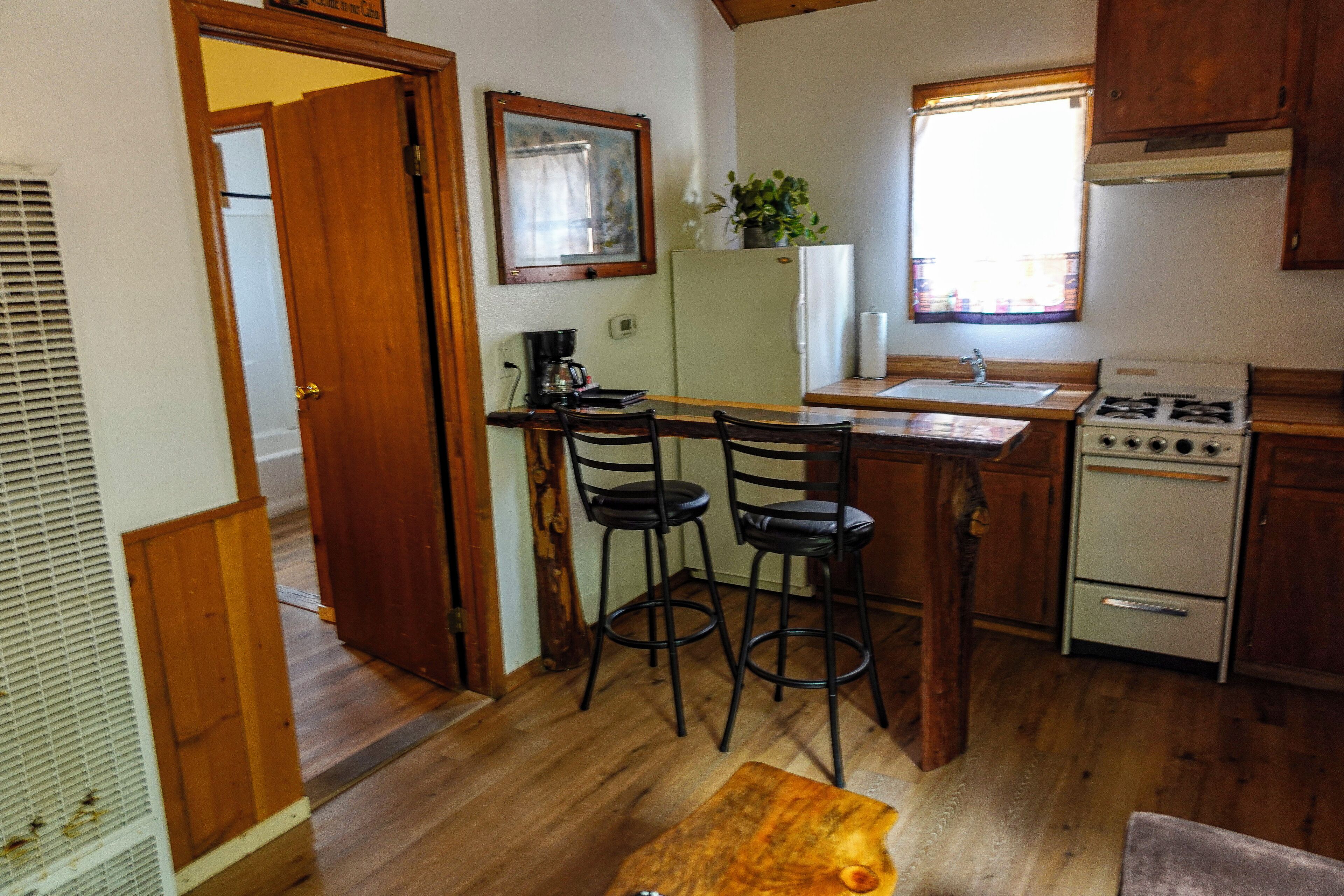Une cuisine compacte avec des meubles en bois, une cuisinière à gaz, un réfrigérateur et un tabouret de bar.