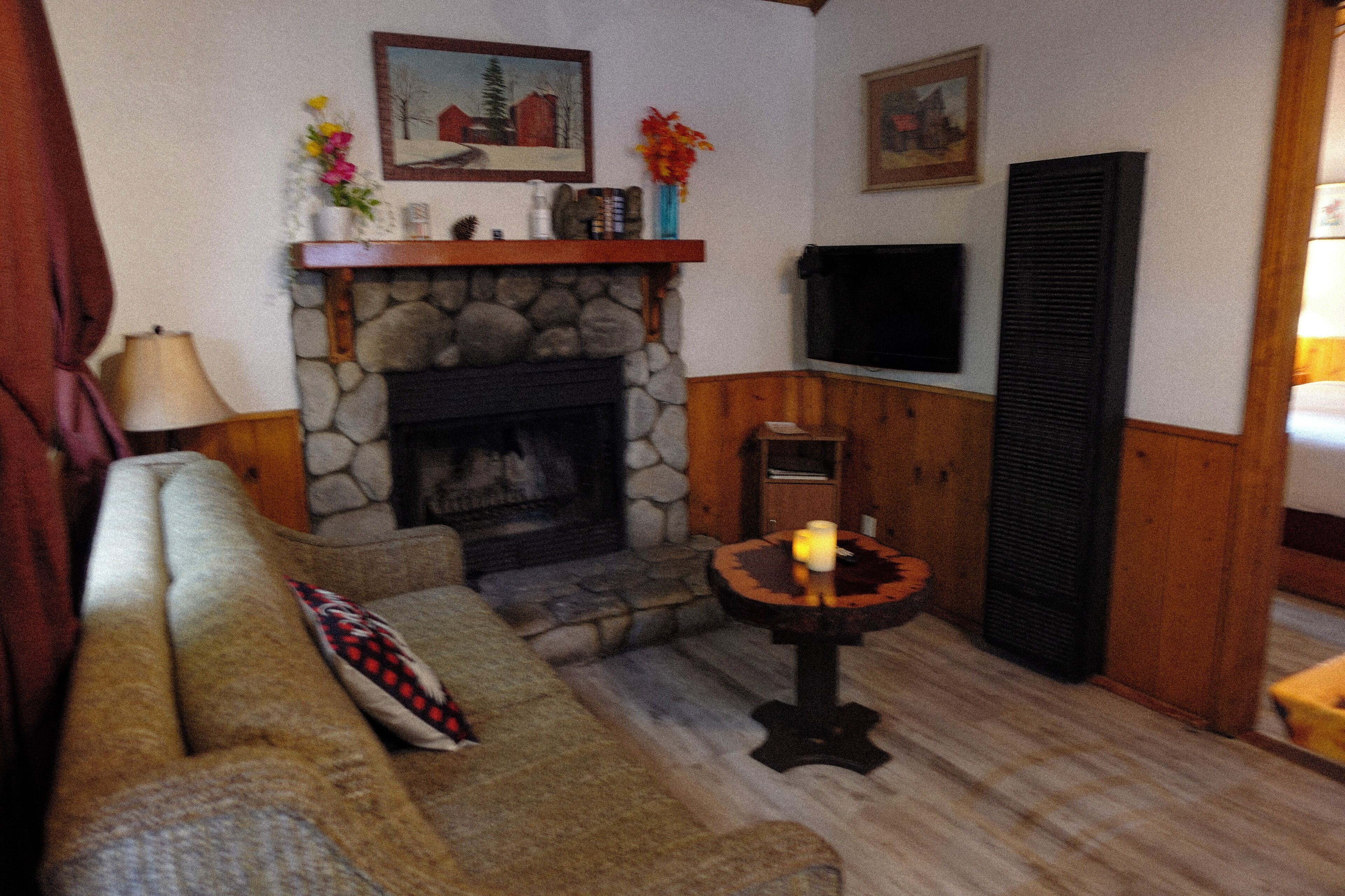 Ein gemütliches Wohnzimmer mit Kamin aus Stein, einem an der Wand befestigten Fernseher und einer hölzernen Bank.