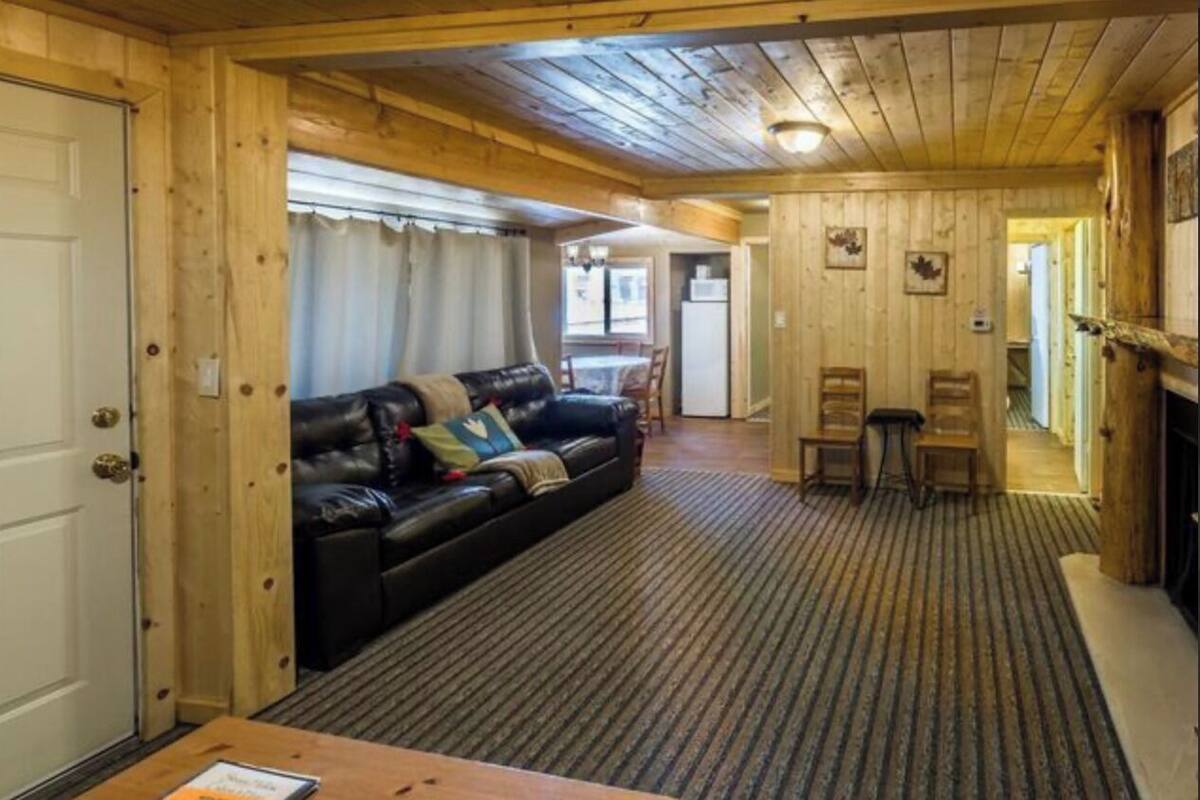 Ein gemütliches Blockhaus-Interieur mit einem schwarzen Ledersofa, einer Essecke mit zwei Stühlen und einem Kamin.