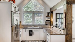 A modern kitchen with white cabinetry, a large window, and a stone countertop. - Breck_diamond_view (Breckenridge)
