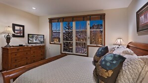A bedroom with a large bed, a dresser, a television, and a window with a view of a snowy landscape. - Beaver_creek_chalet_verve (Avon)