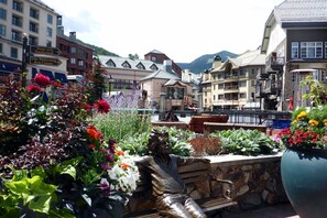 Une place agrémentée d’une statue, de bancs et de parterres de fleurs.