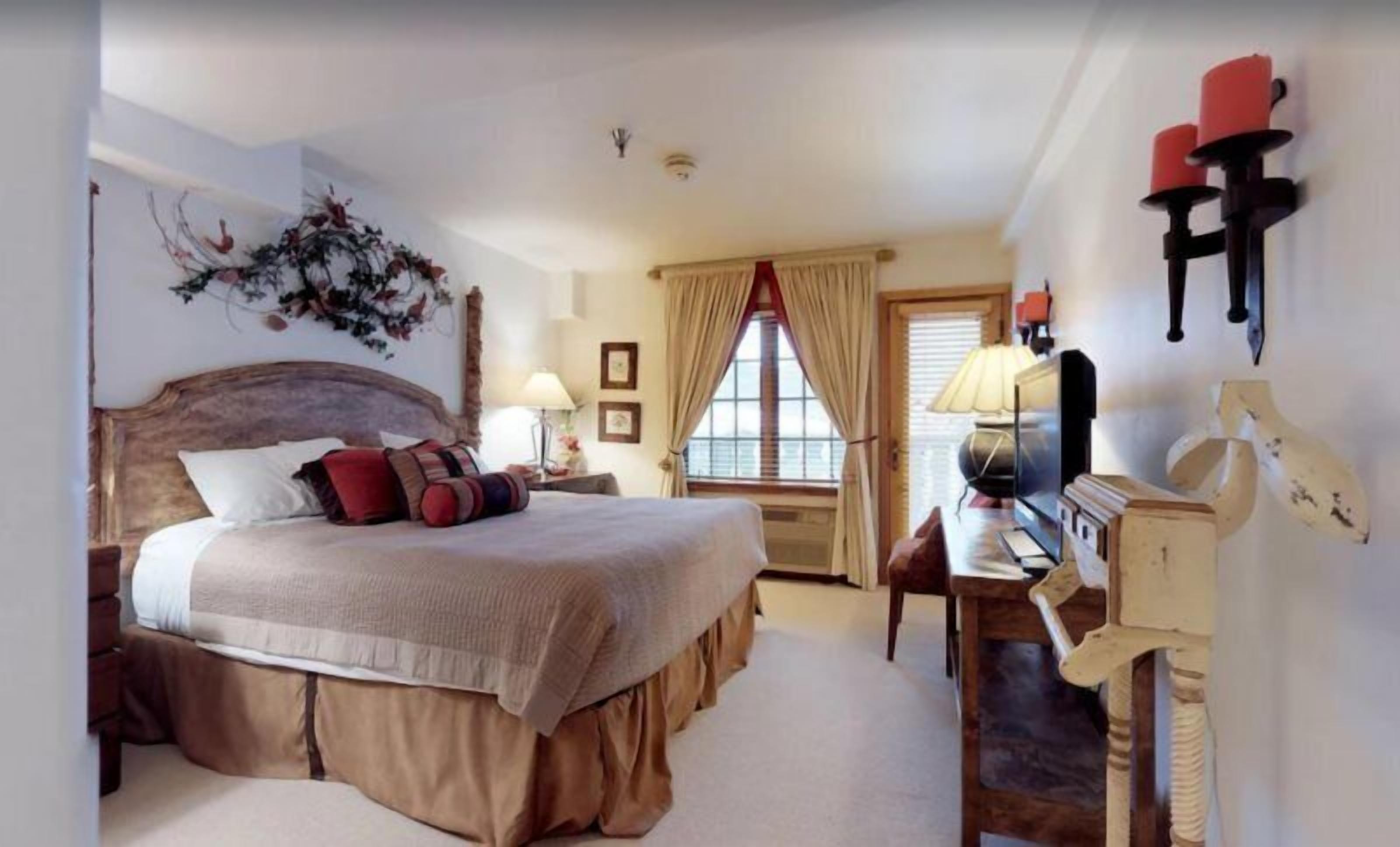 A bedroom with a large bed, a desk with a lamp, and a window with curtains.
