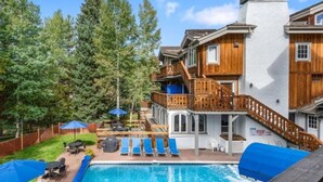 A pool area with lounge chairs and umbrellas, surrounded by a wooden deck and a white building with balconies. - Vail Bridge Street 3 Bedroom Condo (Vail)