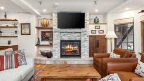 A living room with a stone fireplace, leather sofas, a wooden coffee table, and a flat-screen TV mounted above the fireplace. - Vail Bridge Street 3 Bedroom Condo (Vail)