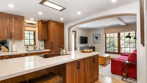 A modern kitchen with wooden cabinets, a large island, and a dining area with a red sofa. - Vail Bridge Street 3 Bedroom Condo (Vail)
