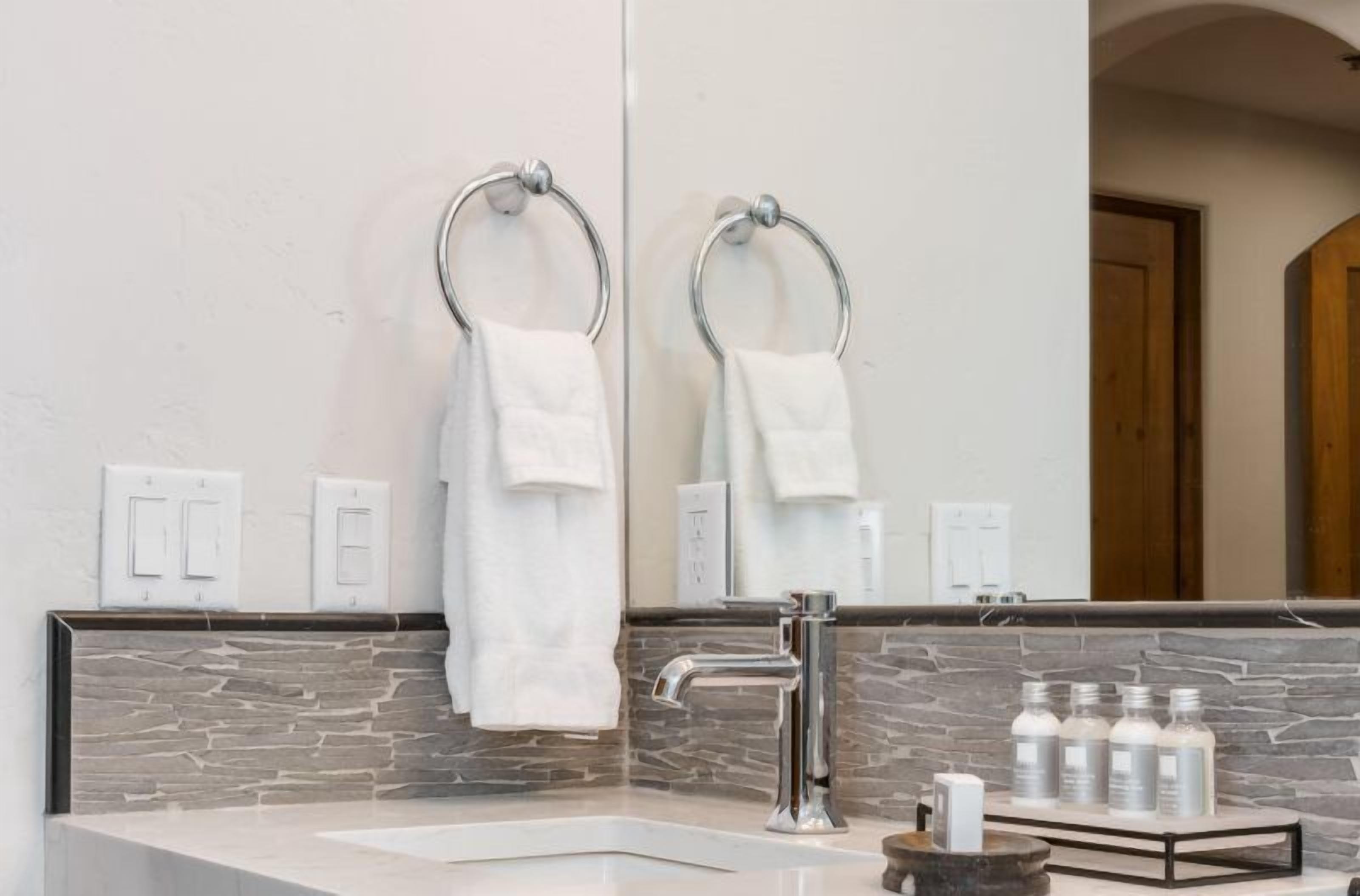 A modern bathroom with a stone backsplash, a large mirror, a chrome faucet, and a towel rack.