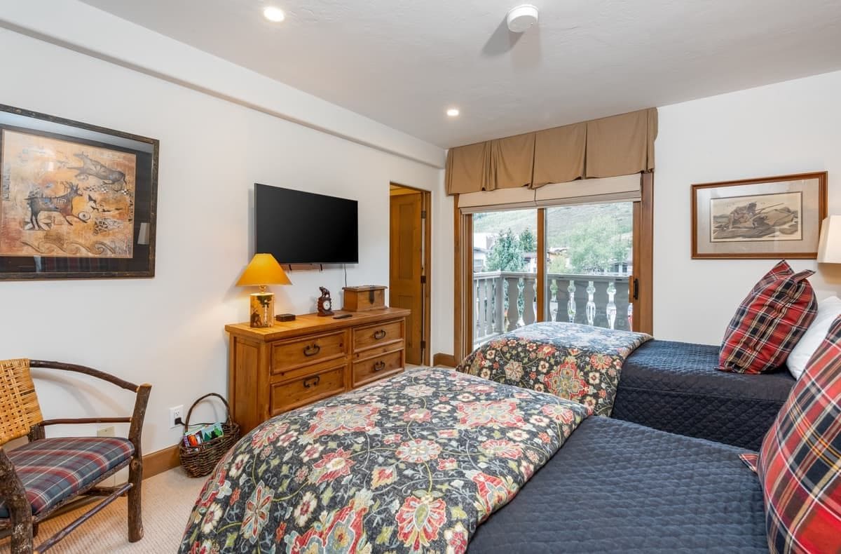 A bedroom with a bed, a television, a wooden dresser, a chair, and artwork on the walls.