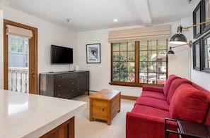 Una sala de estar con un sofá rojo, una mesa de centro de madera, un televisor y un ventanal con vistas.