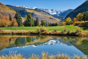Un lago tranquilo con un reflejo claro, rodeado de árboles de colores otoñales y montañas al fondo.