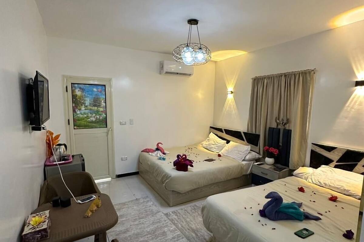 Ein Hotelzimmer mit zwei Betten, einem Schreibtisch, einem Stuhl, einem Fernseher und einer Klimaanlage.