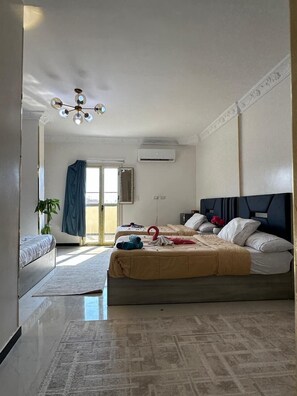 Ein Hotelzimmer mit einem großen Bett, einer Deckenleuchte, einer Klimaanlage und Blick durch eine Tür.