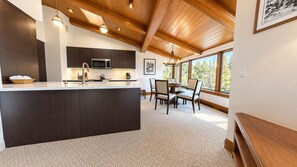 A modern kitchen with a central island, dark cabinetry, and a large window providing a view of the outdoors. - Vail Village Plaza Lodge 2 Bedroom Plus Loft (Vail)