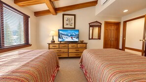 A bedroom with two beds, a dresser, a television, and a window with blinds. - Vail Village Plaza Lodge 2 Bedroom Plus Loft (Vail)