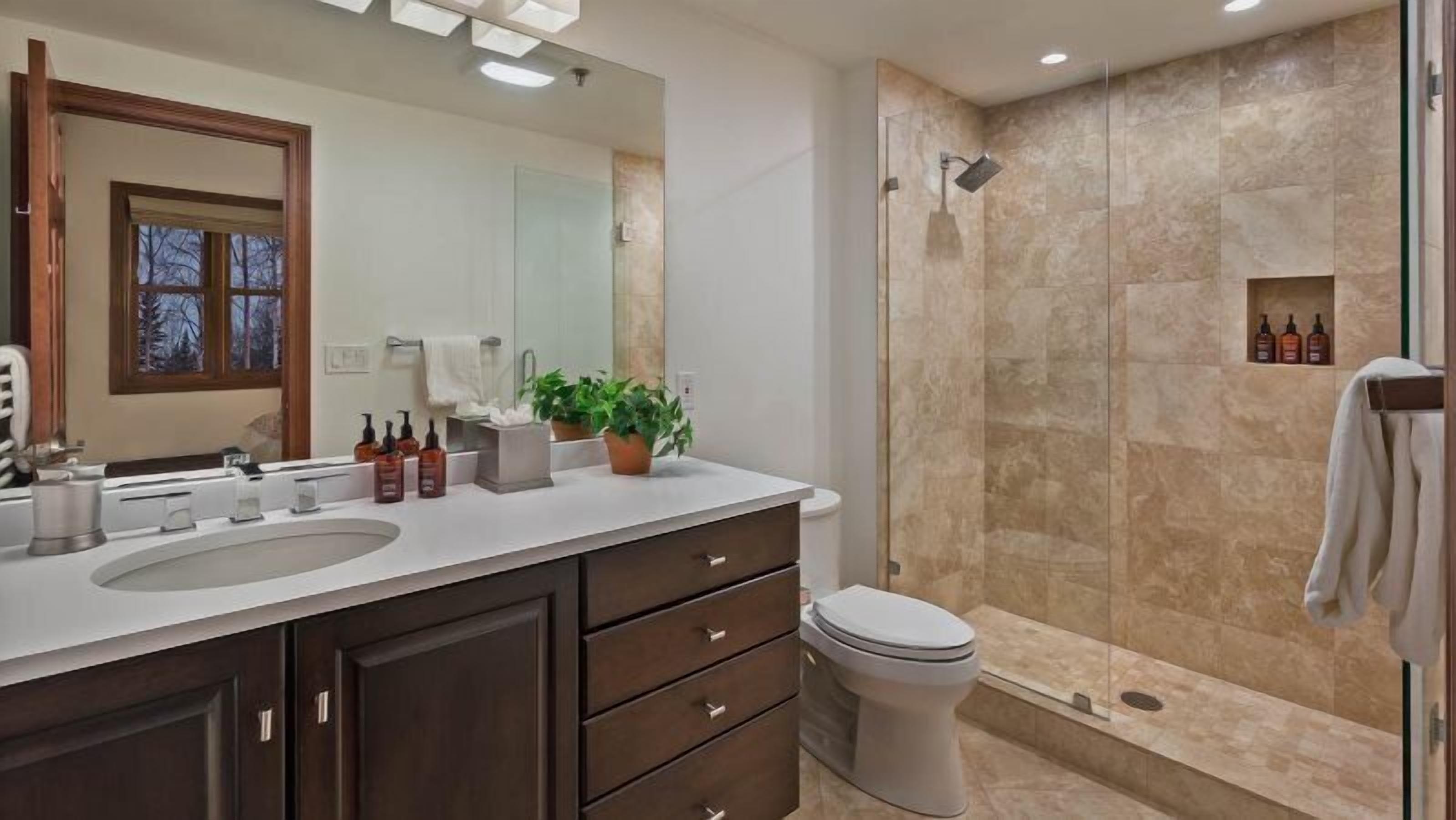 A modern bathroom with a large mirror, dual sinks, a toilet, and a walk-in shower.