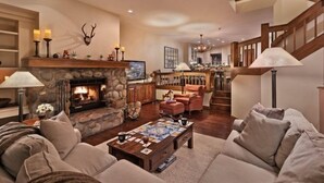 A cozy living room with a stone fireplace, comfortable seating, and a staircase leading to an upper level. - Beaver_creek_chalet_fortessa (Avon)