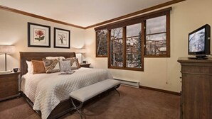 A bedroom with a large bed, a bench, a TV, and a window with a snowy view. - Beaver_creek_chalet_fortessa (Avon)