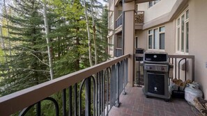 Un balcon doté d’un barbecue et d’une bouteille de propane, entouré d’arbres.