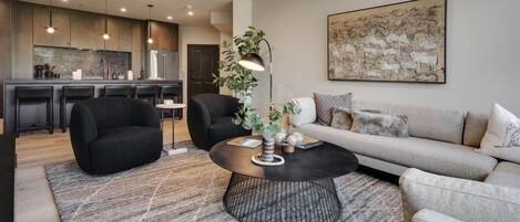 A modern living room with a round coffee table, black and grey sofas, and a large abstract painting on the wall.