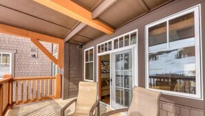 A covered patio with three beige chairs, a wooden railing, and large windows offering a view of a snowy landscape. - One Ski Hill Place 2 Bedroom Luxury Condo (Breckenridge)