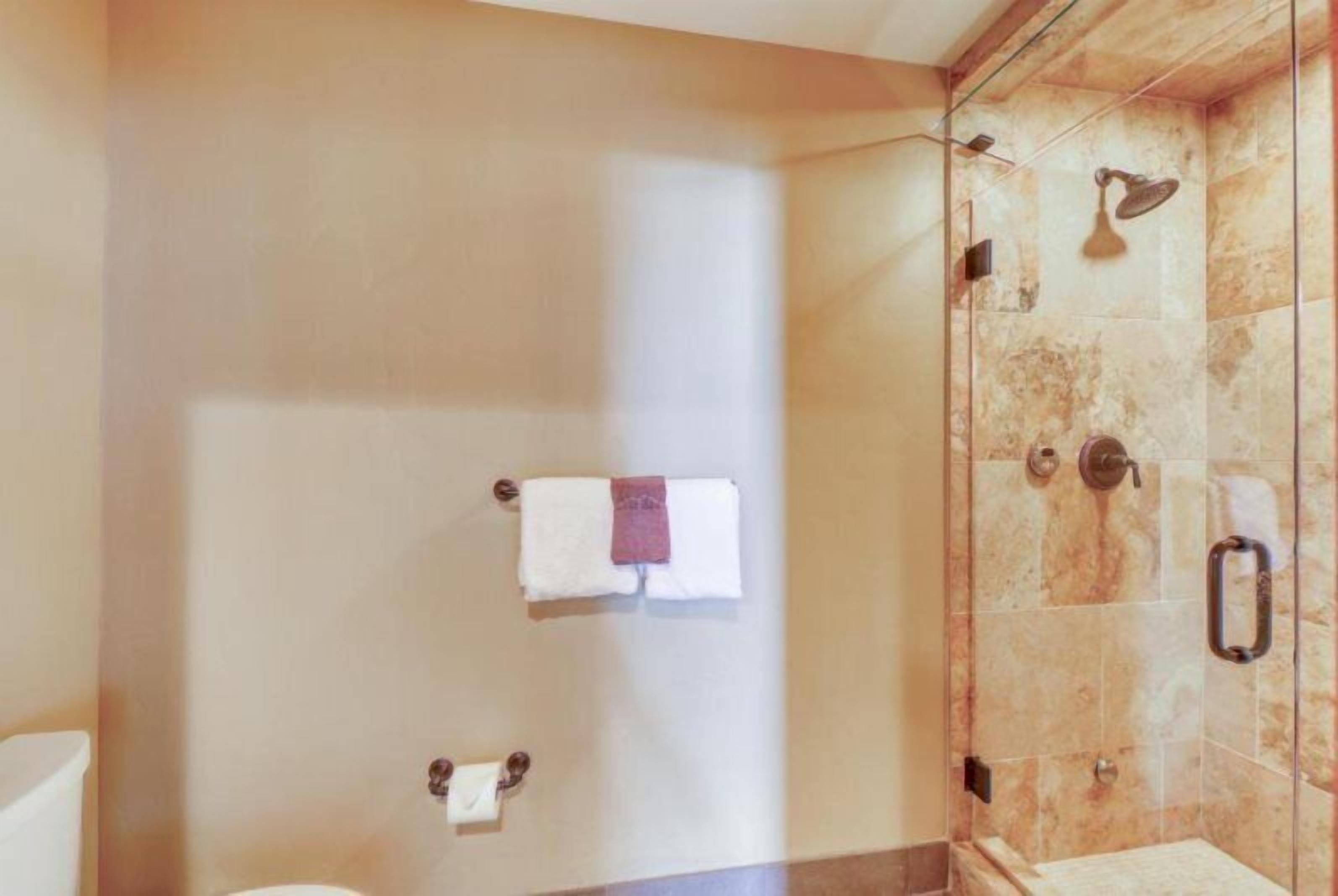 A bathroom with a glass-enclosed shower, marble walls, and a towel rack with a purple towel.