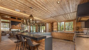 Une cuisine moderne dotée d’un grand îlot central, de tabourets de bar et d’un coin repas offrant une vue sur l’extérieur.