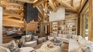 Un vaste espace de vie doté d’un haut plafond et de poutres apparentes, aménagé avec des canapés et une table basse, et une cuisine visible au fond.