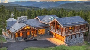 Une grande cabane en rondins à plusieurs étages, dotée de fondations en pierre, de grandes fenêtres et d’un balcon bien visible.