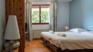 A bedroom with a bed, a nightstand with a lamp, a window with curtains, and a radiator. - SEVRIER, Maison , VUE Panoramique sur le lac et montagnes, 8pers (Sévrier)