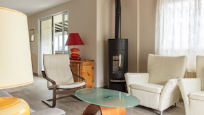 A living room with a glass-top coffee table, two white leather chairs, a red lamp, a wooden cabinet, and a black wood-burning stove. - SEVRIER, Maison , VUE Panoramique sur le lac et montagnes, 8pers (Sévrier)