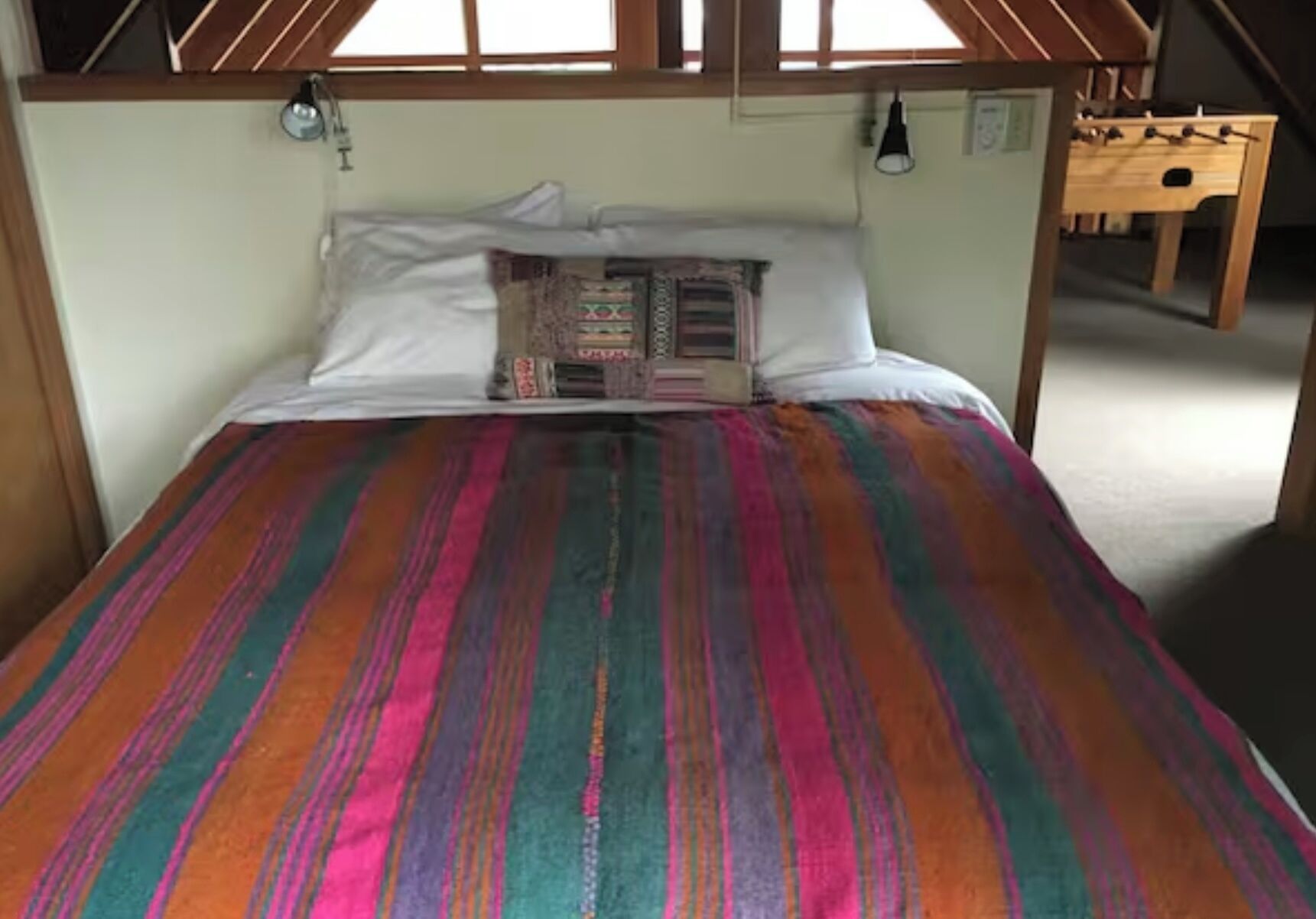Een bed met een kleurrijke gestreepte deken, witte kussens en een hoofdbord met een raam erboven.
