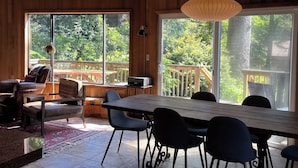 Una habitación amplia con ventanas grandes, techo de madera y un comedor con sillas y mesa.