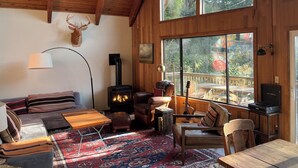 Un salón acogedor con chimenea, muebles de madera y ventanas amplias que ofrecen vistas al exterior.