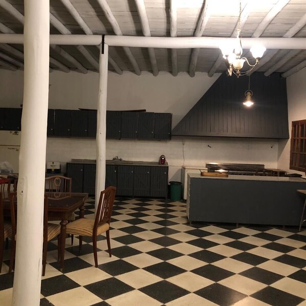 Une pièce avec un sol à carreaux, des chaises en bois, une table et un coin cuisine équipé de placards et d’une cuisinière.