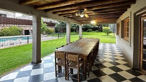 Un'area pranzo all'aperto coperta, con pavimento a scacchi e tavolo di legno con sedie.