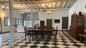 Un'ampia stanza con pavimento a scacchi, tavolo da pranzo in legno, sedie, lampadari e un grande armadio.