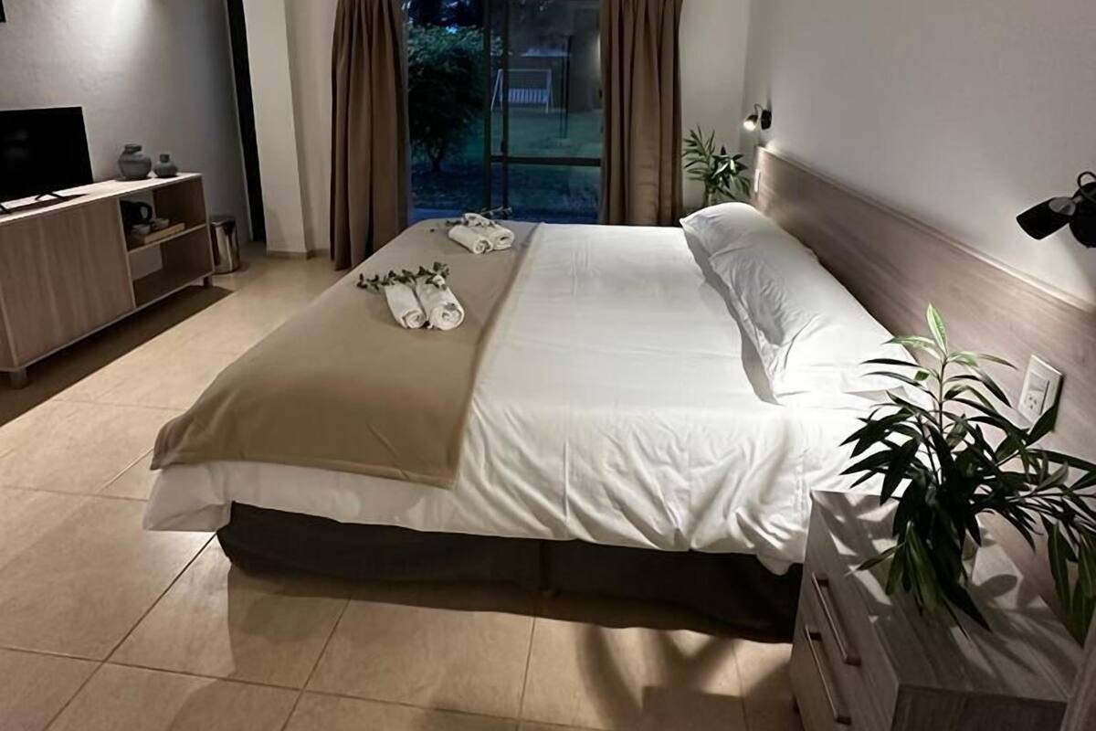 A hotel room with a bed, a TV, a desk, and a window with curtains.