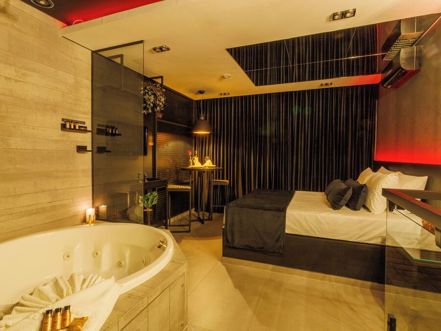 Una habitación de hotel moderna con una bañera grande, una cama con ropa oscura y un separador de vidrio.