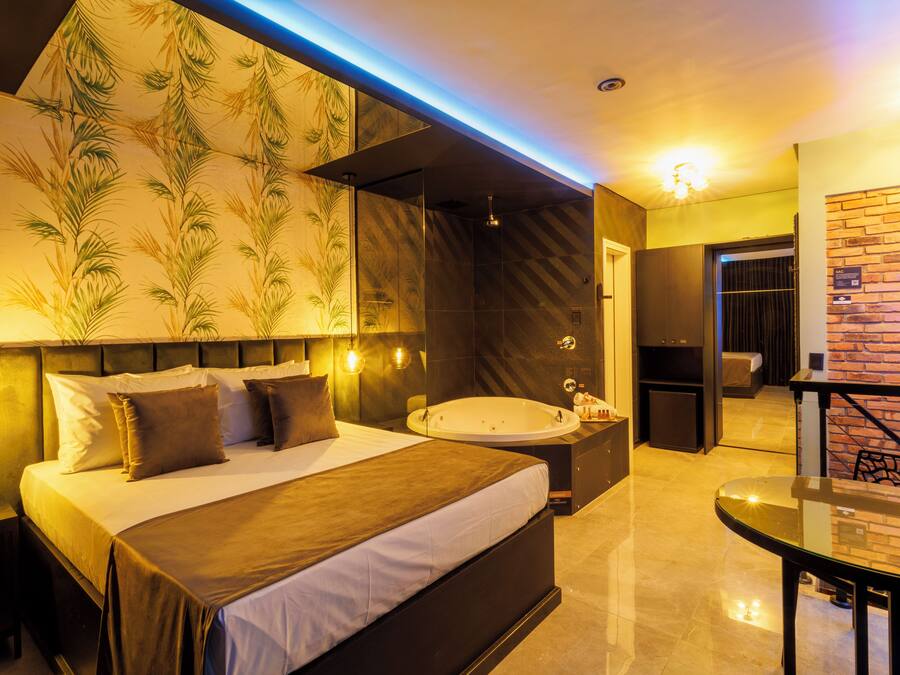 A modern hotel room with a large bed, a separate bathroom, a sitting area with a table, and a brick wall.