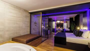 A modern hotel room with a glass-enclosed shower, a large bathtub, a sofa, and a bed.