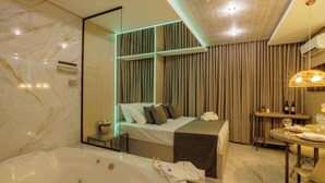 A modern hotel room with a large bed, a separate sofa, a dining area, and a separate bathroom with a bathtub. - Medieval Motel SPA (Porto Alegre)