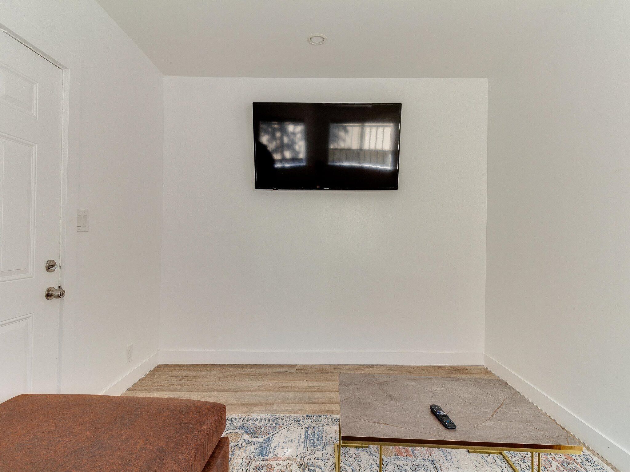 A room with a wooden floor, a brown sofa, a small table, and a mounted TV on the wall.