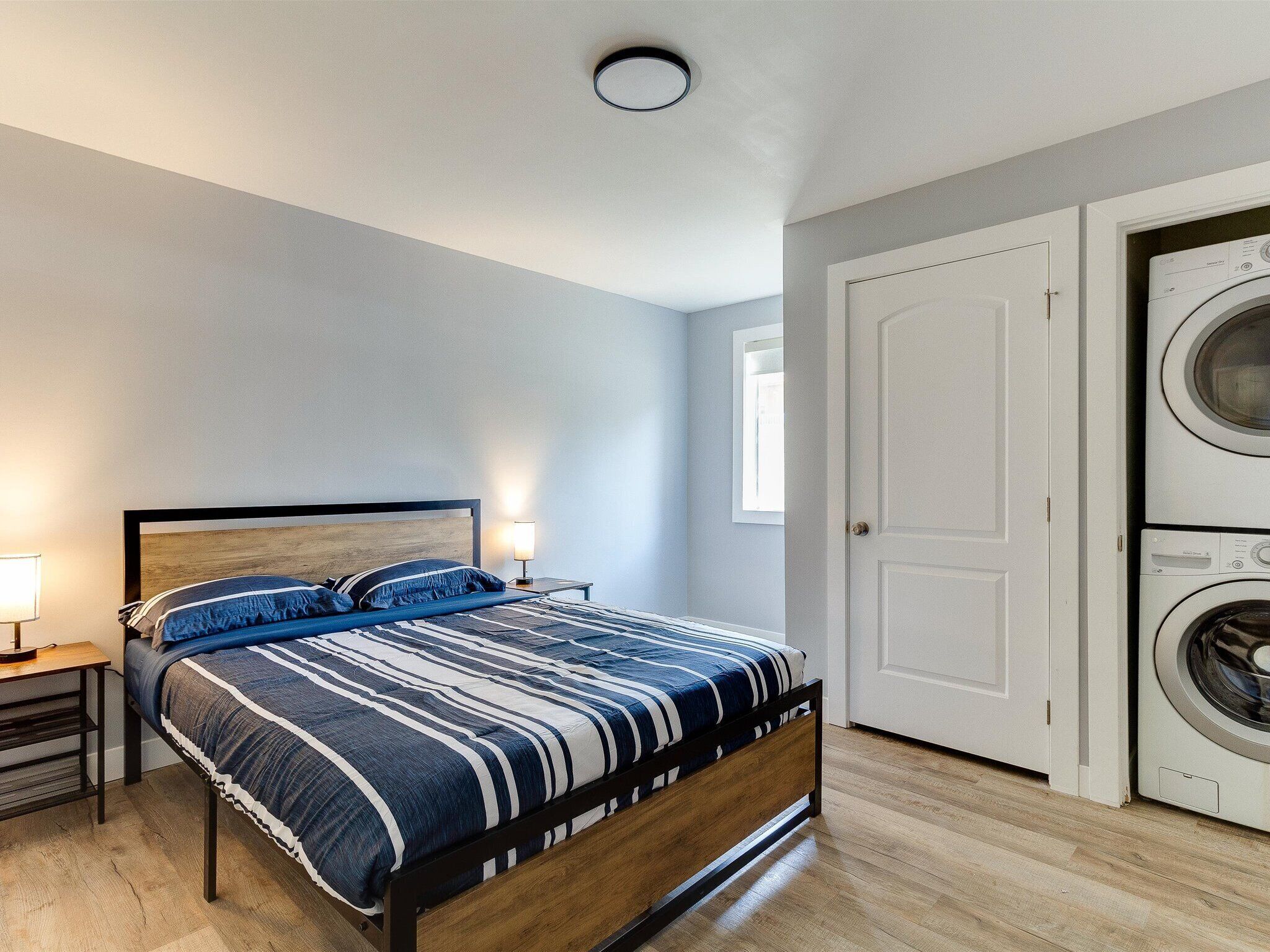 A bedroom with a bed, nightstand, lamp, and a washing machine.