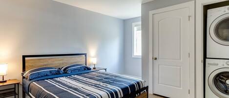 A bedroom with a bed, nightstand, lamp, and a washing machine.