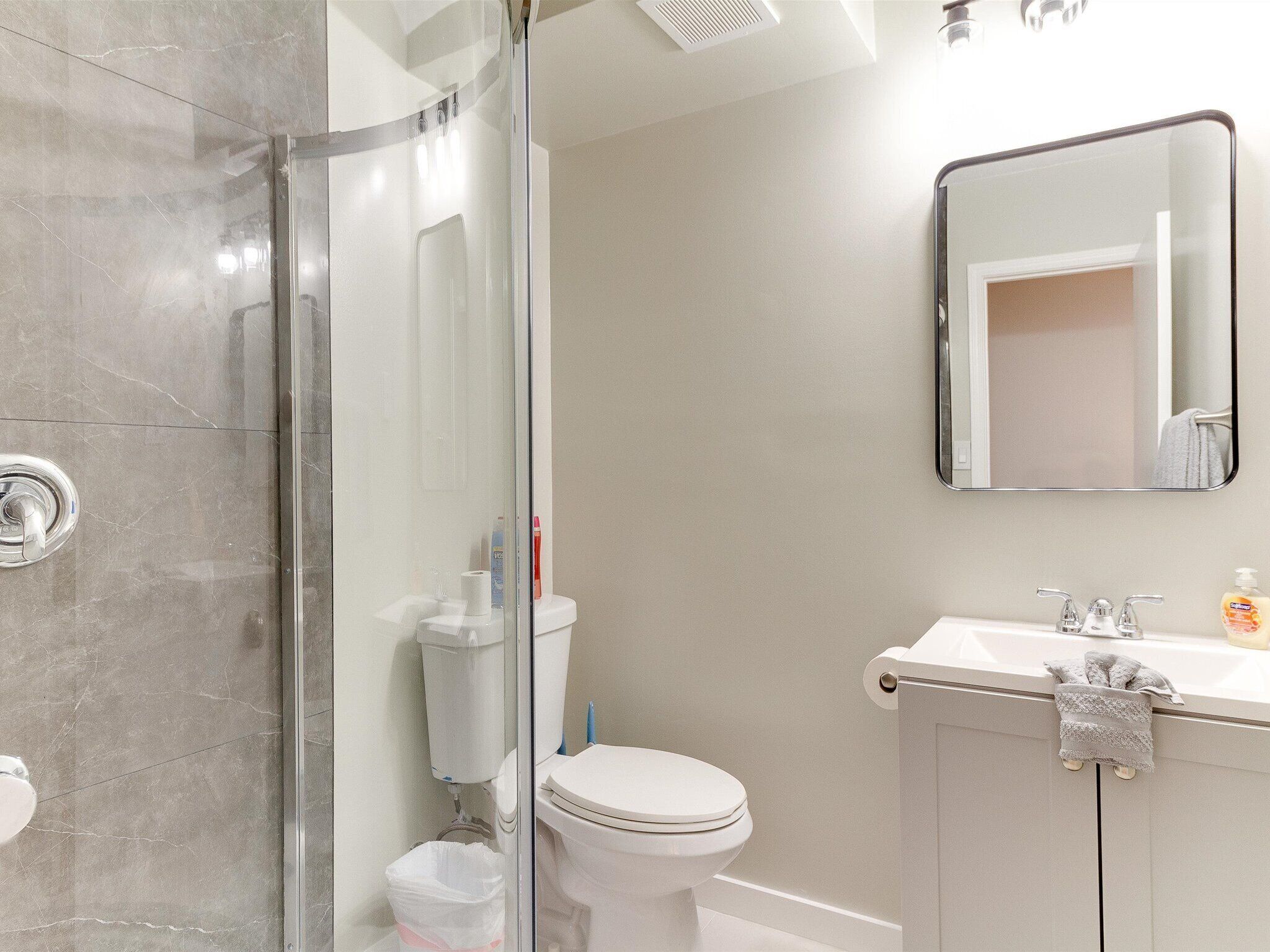 A bathroom with a glass-enclosed shower, a toilet, and a sink with a mirror above it.